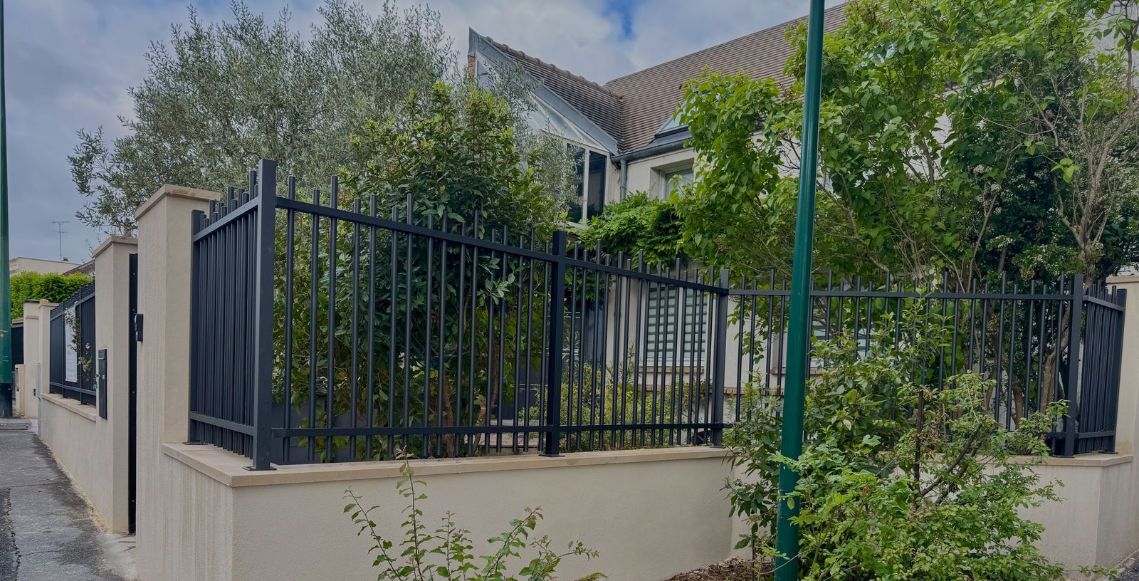 Clôture en aluminium noir à barreaux sur muret enduit, à l'angle d'une rue