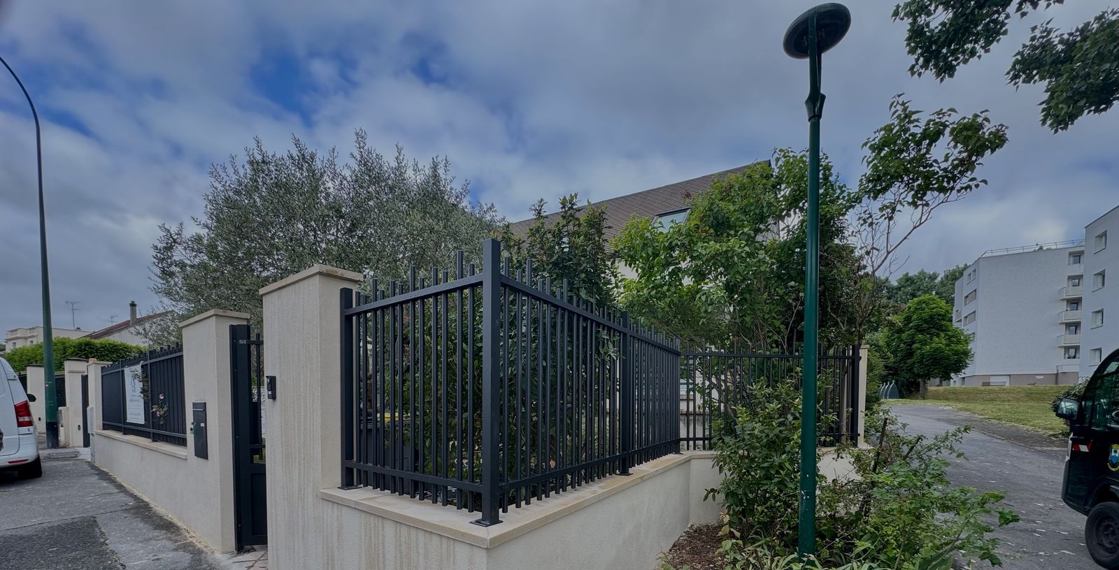 Clôture en aluminium noir à barreaux sur muret, le long d'une rue