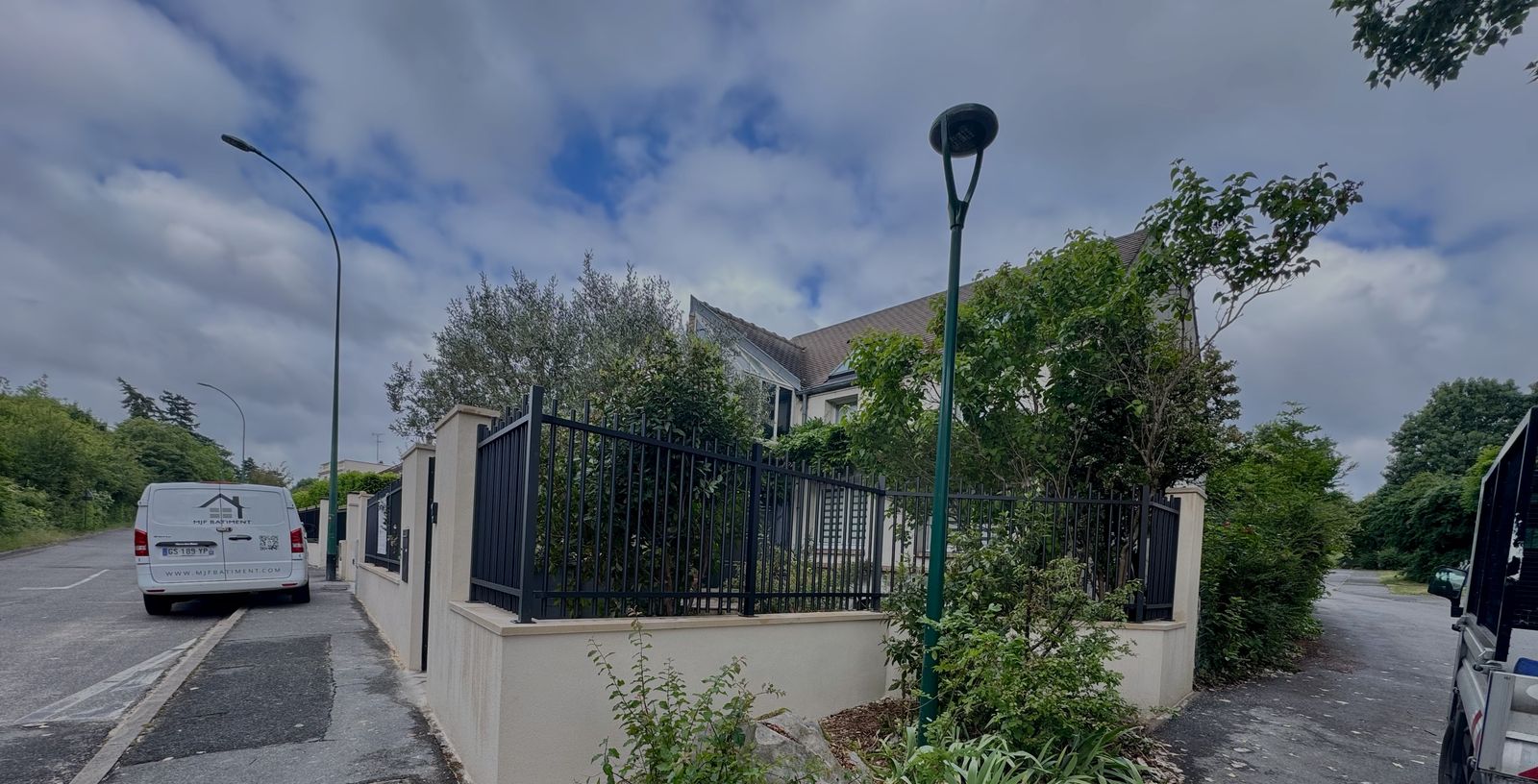 Clôture en aluminium noir à barreaux sur muret enduit, au coin d'une rue
