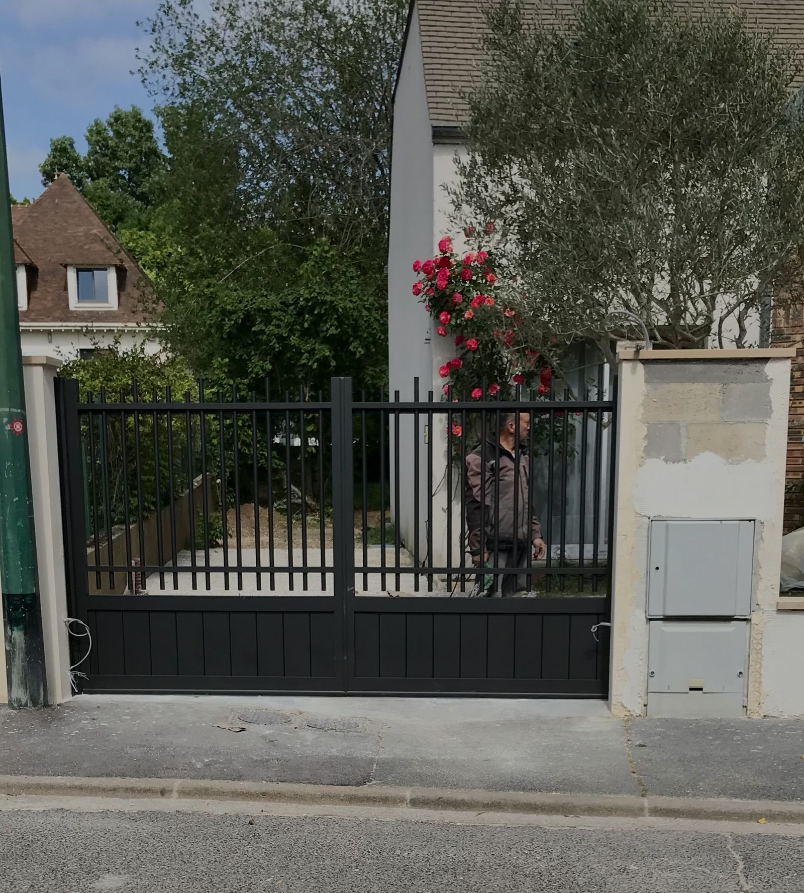 Portail battant deux vantaux en aluminium noir, barreaux verticaux et soubassement plein, entre piliers